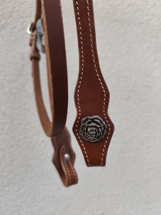 Zbliżenie Spanish-cut końcówki policzka ogłowia PROLINE — ręcznie grawerowana concha z motywem róży antyczne srebro, skóra kasztan, białe przeszycia — HorsePassion.pl